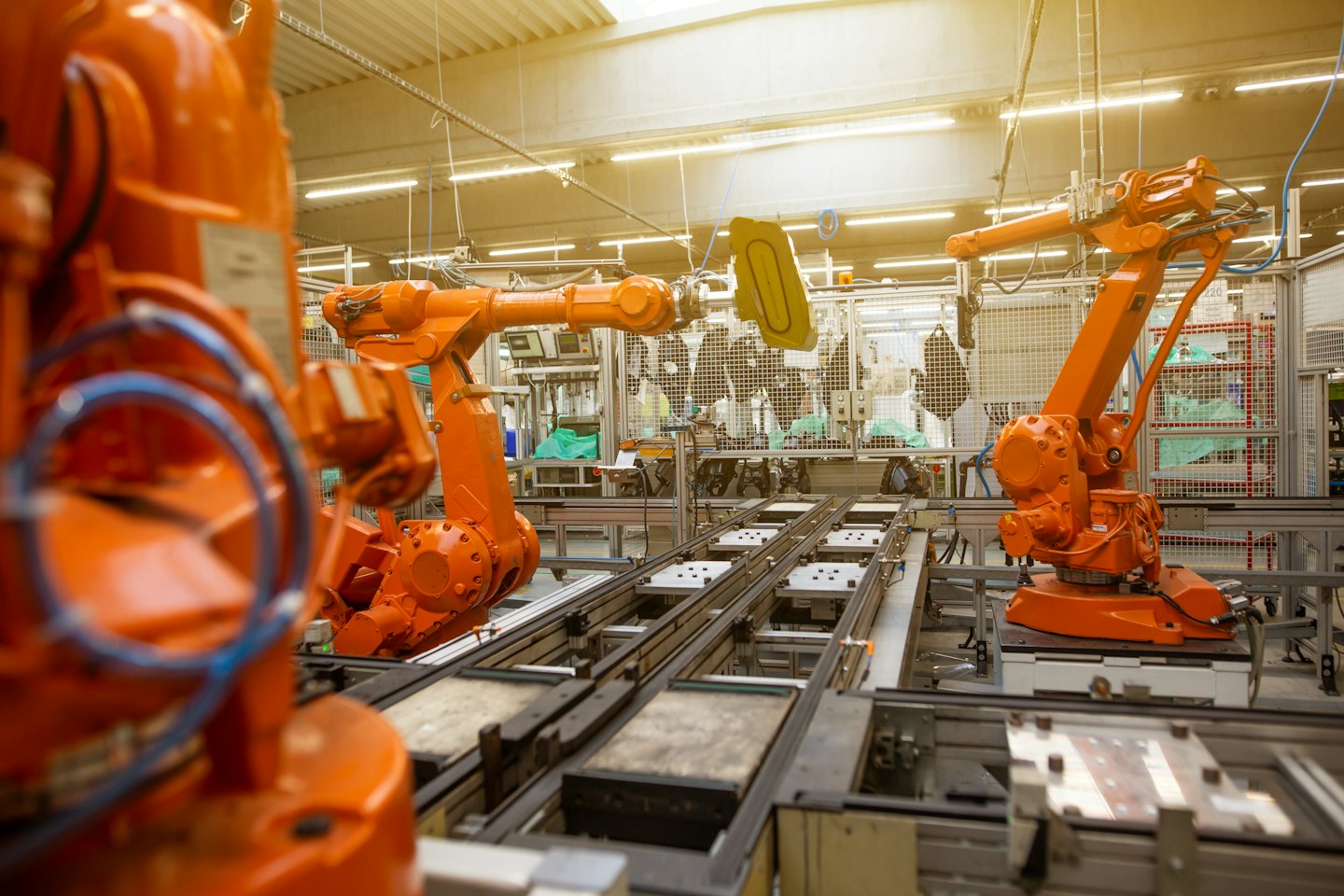 Parlak aydınlatılmış fabrika zemininde robotik kollar bileşenleri monte ediyor.